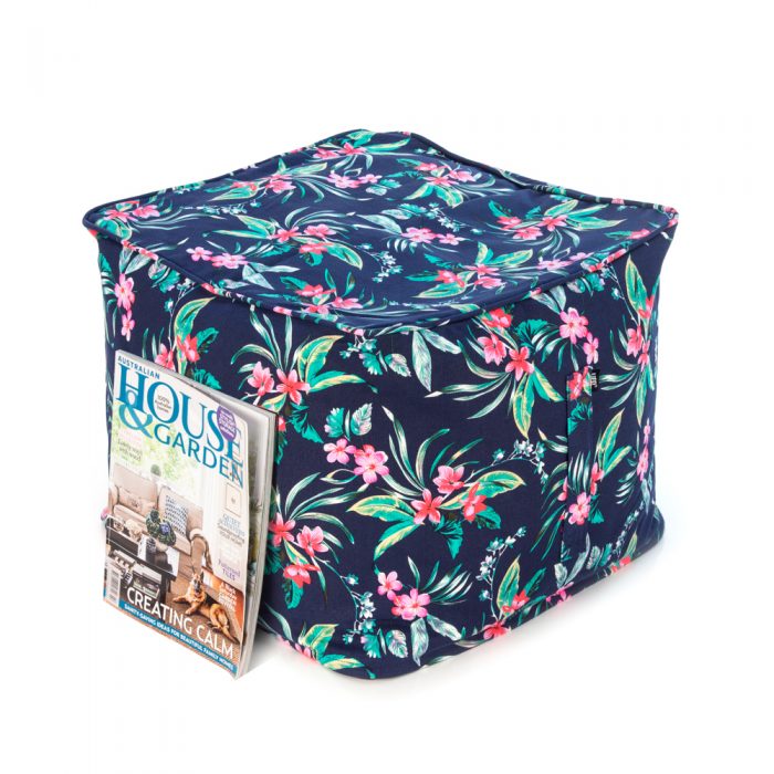 A house and garden magazine rests against a pink and green tropical print on a navy base