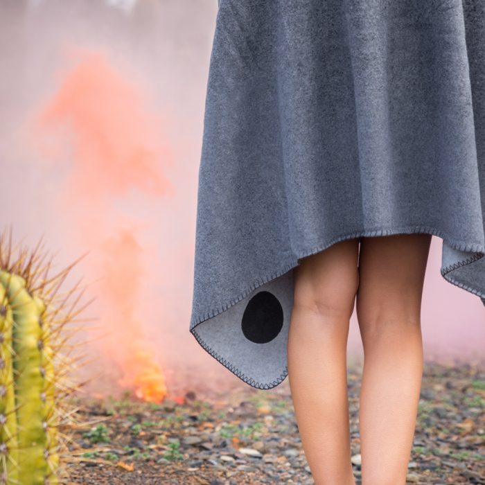 Grey fleece blanket draped around a women showing the stitching detail and a cactus and orange smoke in the background