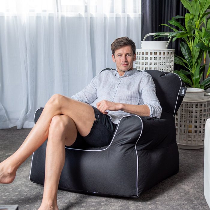 A man sits on a black armchair shaped chillout bean bag