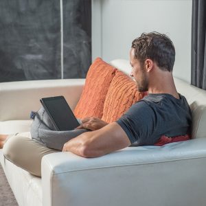 Man sits on a couch using his iPad sitting on a grey linen look iCrib tablet holder bean caddy