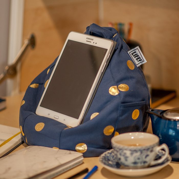 A tablet sits on a navy blue bean filled bean caddy with gold coin spots. A cup or tea, teapot and journal are visible.