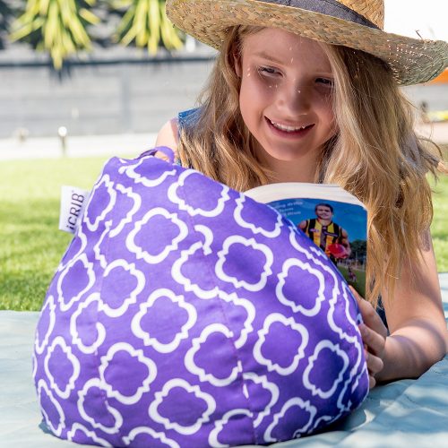 A teen reads a book resting on a purple iCrib bean bag with a white geometric print.