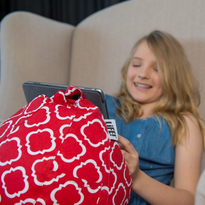 A teen watches her iPad nestled in a red iCrib with white geometric print.