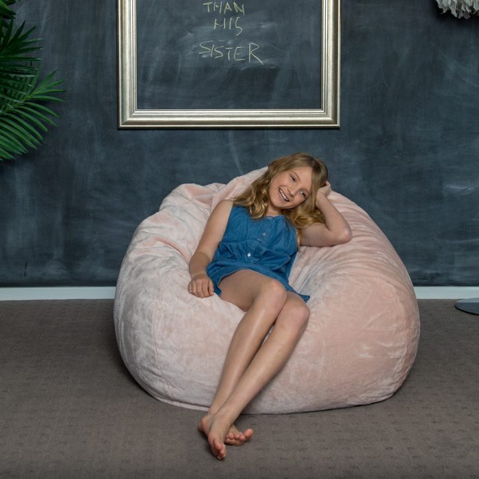 Teen reclines on the super size peach pink faux fur tear drop shaped bean bag