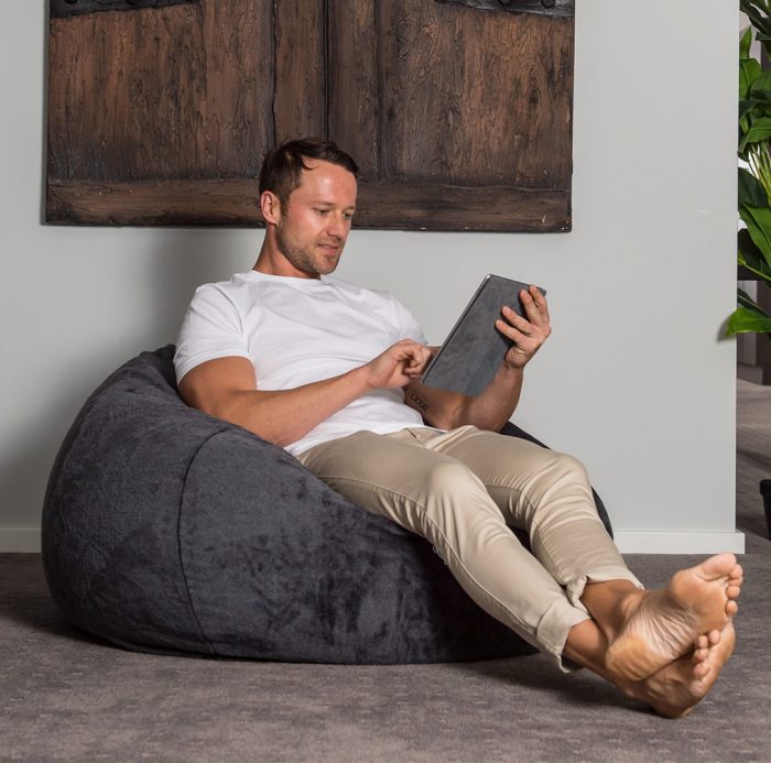 Man sits in the slate grey faux fur super size tear drop bean bag working on his ipad