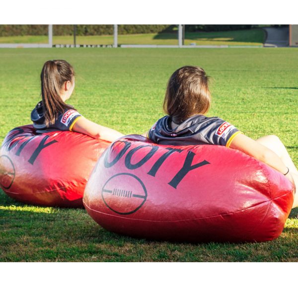 Two women sitting on large football bean bags on a grass football oval