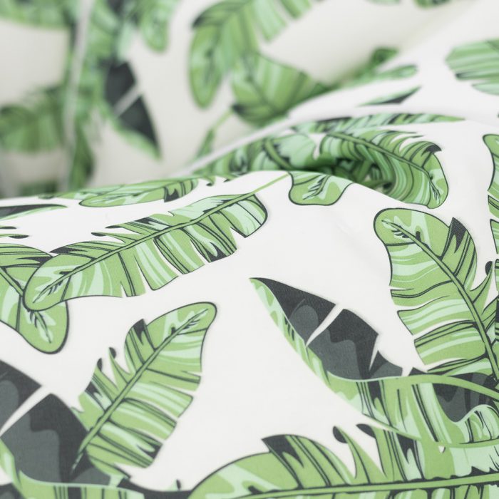 Close up of the tiki print with green montserrat palm leaves on a white background