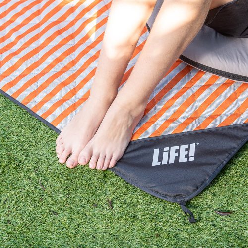 A teens feet sit on the edge of a retro striped picnic blanket with the LiFE! logo visible on the privacy pocket