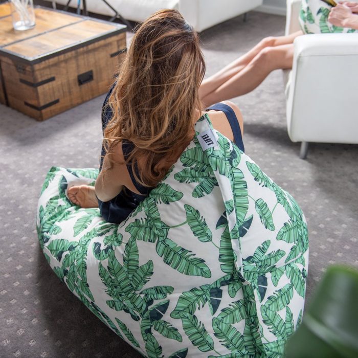 A woman sits on a leaf print luna bean bag in her home. The LiFE! branded tag can be seen