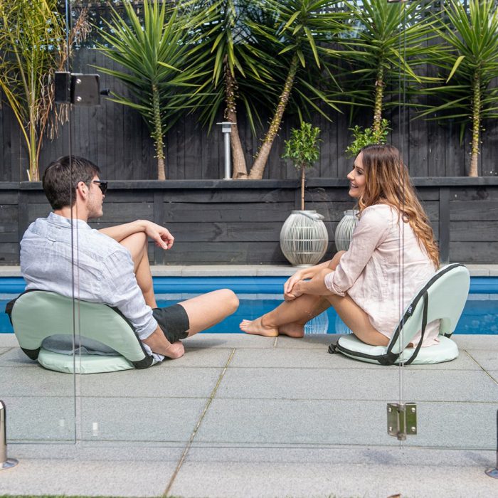A couple sit poolside on tropical green cushion recliners