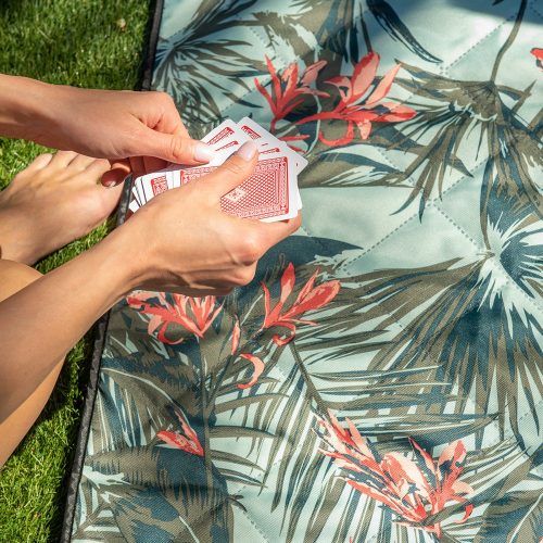 A women deals cards above a tropical print close up of a adventure mat picnic rug