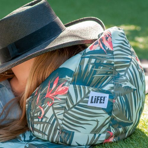 A girl snoozes on a waikiki print iCrib outdoors. The LiFE! branded tag is visible on the storage pocket