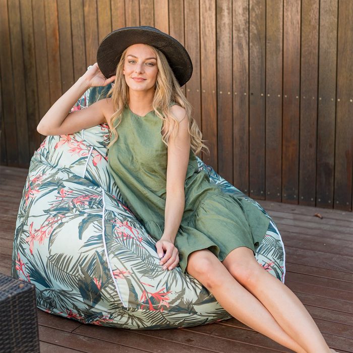 A woman sits in a super size teardrop bean bag on the patio with a tropical floral print