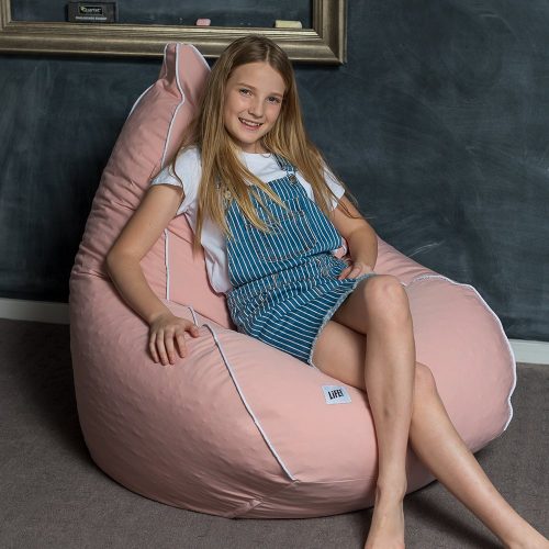 A teen sits on a soft pink coral colored teardrop shaped bean bag with contrast white trim