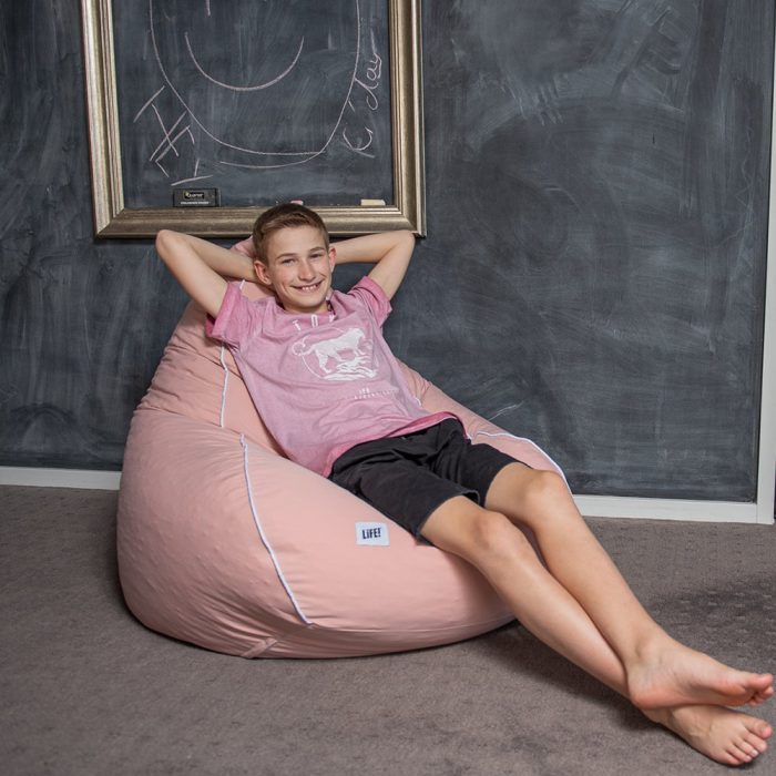 A teen reclines in a coral pink teardrop shaped ban bag